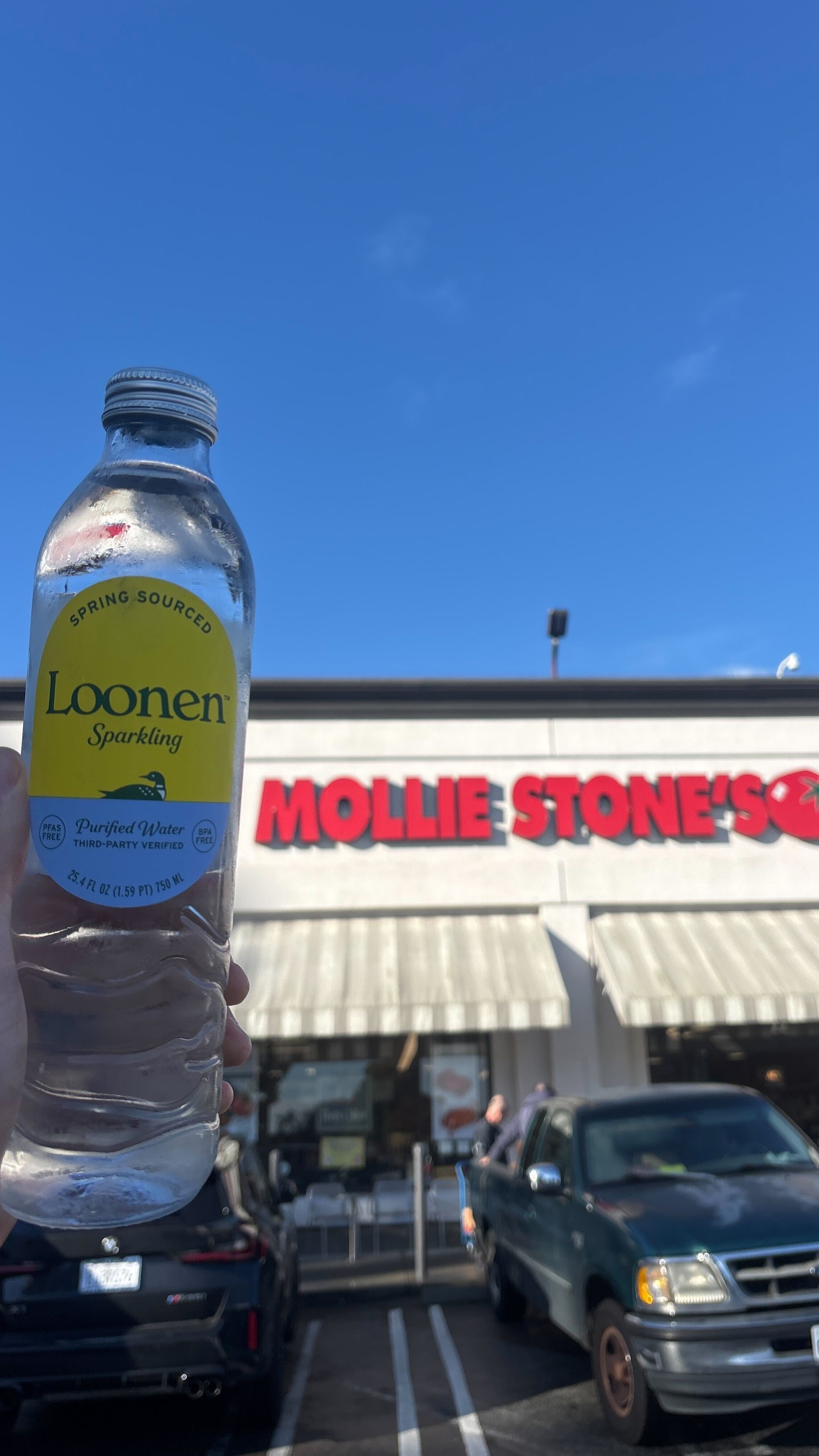 Loonen sparkling water bottle held in front of Mollie Stone's grocery store.